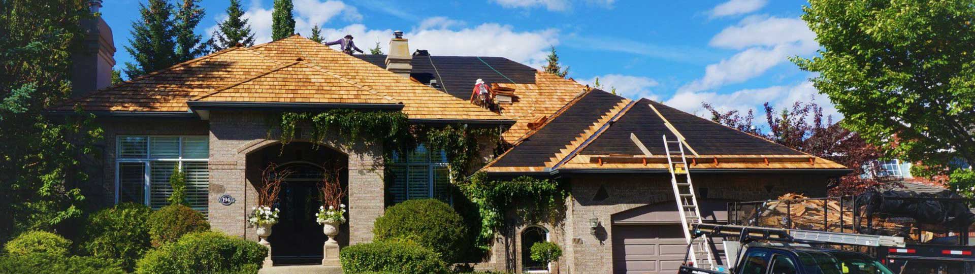 An image of a house undergoing a roof replacement, with new wood shingles being installed.
