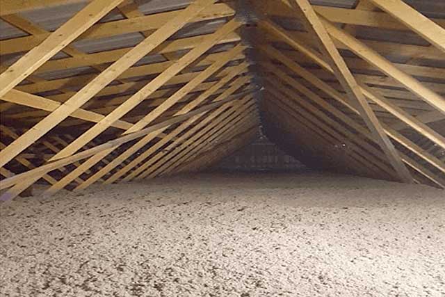 A photo of an attic with new insulation. The attic space is large and open, and the new insulation has been installed on the floor and between the rafters.