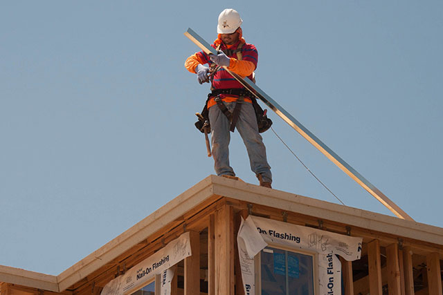 A photo of a roofer preparing for a roof replacement by cutting a piece of wood with a saw.