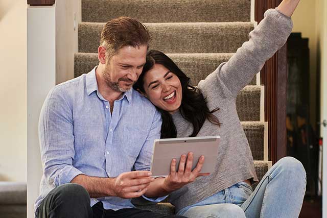 A photo of a couple looking excitedly at a tablet or a digital device.