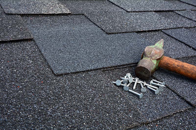 A photo of roofing nails and roofing hammer laying on top of asphalt shingles.